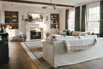 A warm winter living room featuring layered lighting with table lamps, floor lamps, and soft ambient light illuminating beige seating, a fireplace, and seasonal decor | Ocean Pacific Lighting