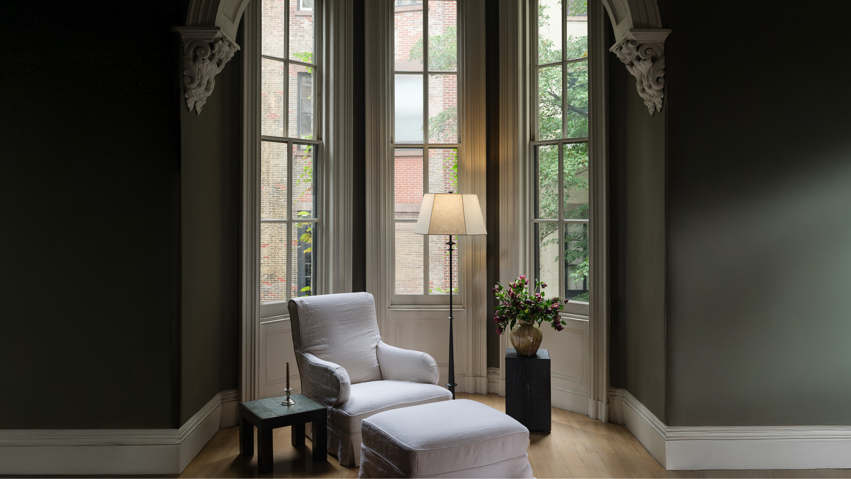 Gray armchair and ottoman in a room with large windows and decorative elements.slider_item_iYAMKd